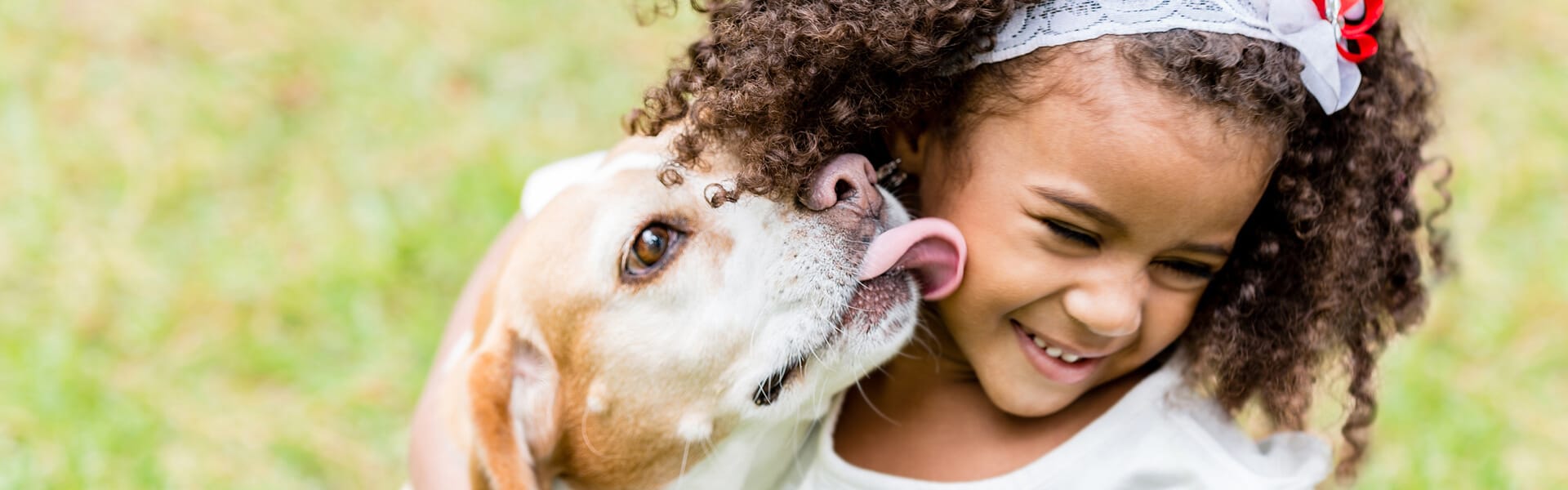 o fetita se joaca cu un catel si acesta incearca sa o linga